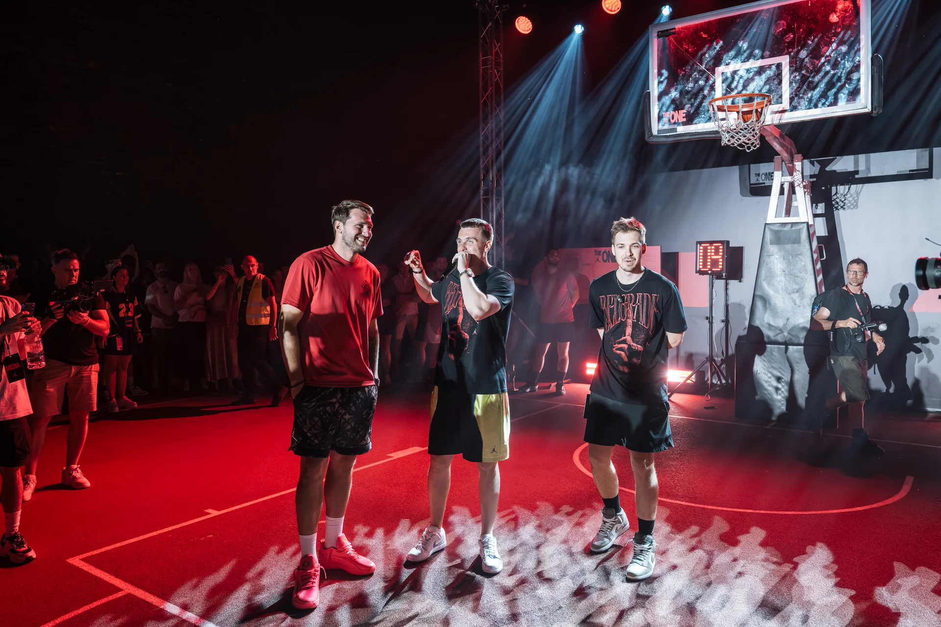 Host speaking into a microphone beside guests under the hoop at Jordan The One in Belgrade
